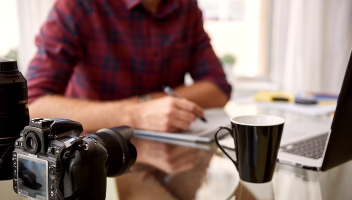 Hombre trabajando en un escritorio con computadora portátil, cámara y café