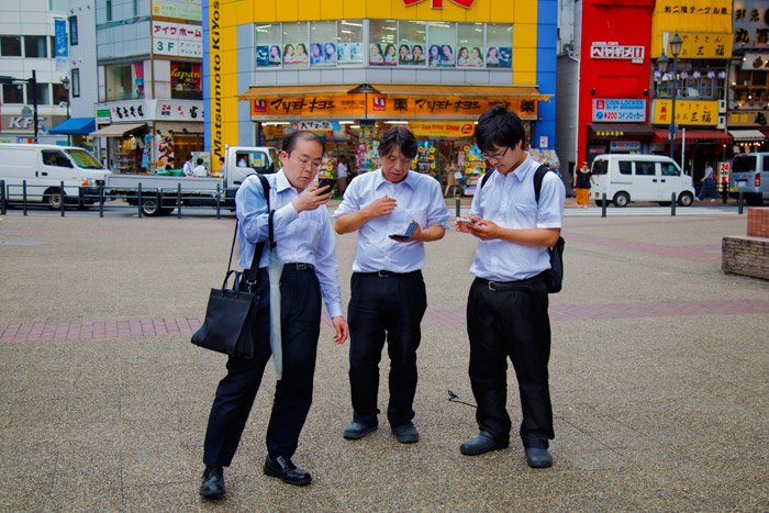 tres hombres mirando sus teléfonos en la calle