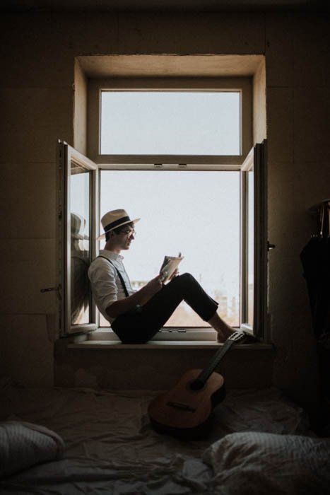 Un hombre sentado en el marco de una ventana leyendo