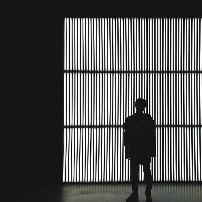 Fotografía en blanco y negro de un hombre parado frente a una ventana rallada