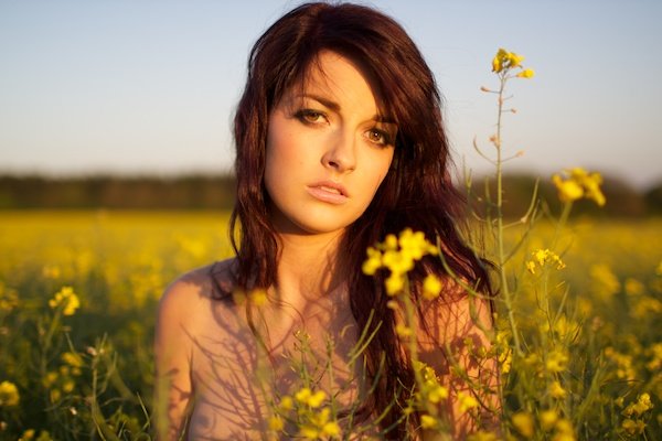 Foto de una mujer joven en el campo de flores amarillas mirando a la cámara.