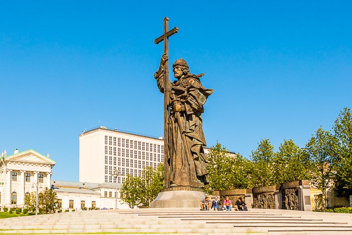 un grupo de personas sentadas debajo de una estatua alta en un día claro y brillante