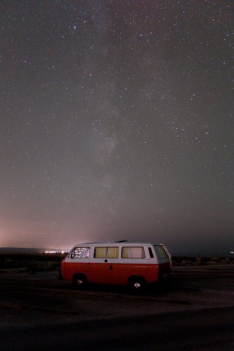 Imagen de una autocaravana roja aparcada bajo un impresionante cielo estrellado