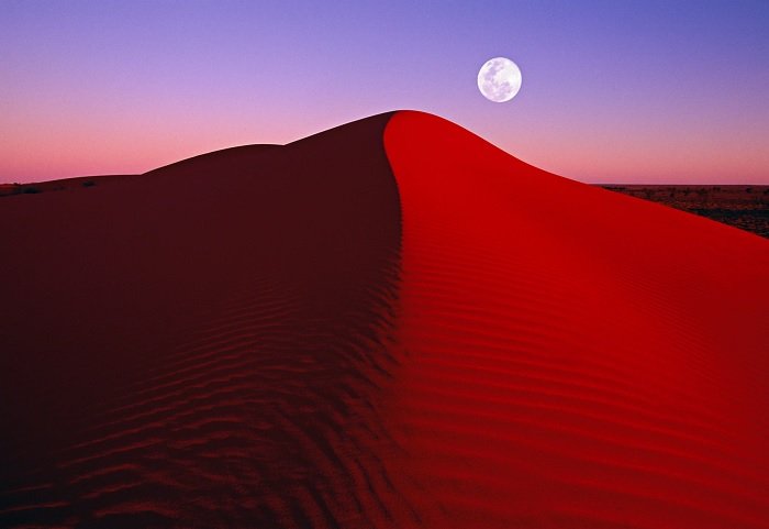 Duna de arena con luna al fondo al atardecer