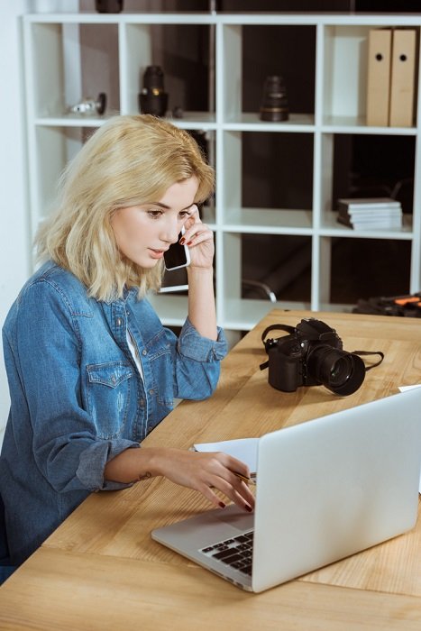 una mujer hablando por su celular mientras mira su laptop