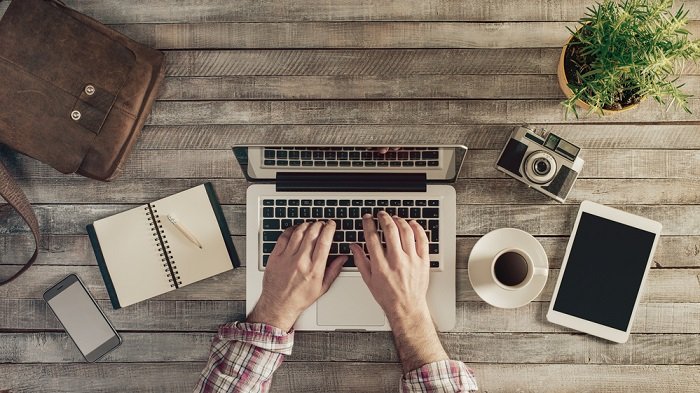 una foto plana de alguien escribiendo en su computadora portátil sobre una mesa de madera
