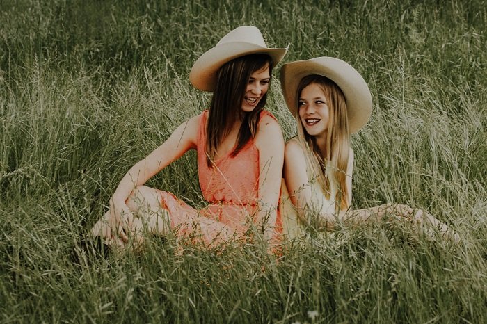 Dos chicas con sombreros de vaquero sentadas en un campo, una idea de sesión de fotos de hermanas