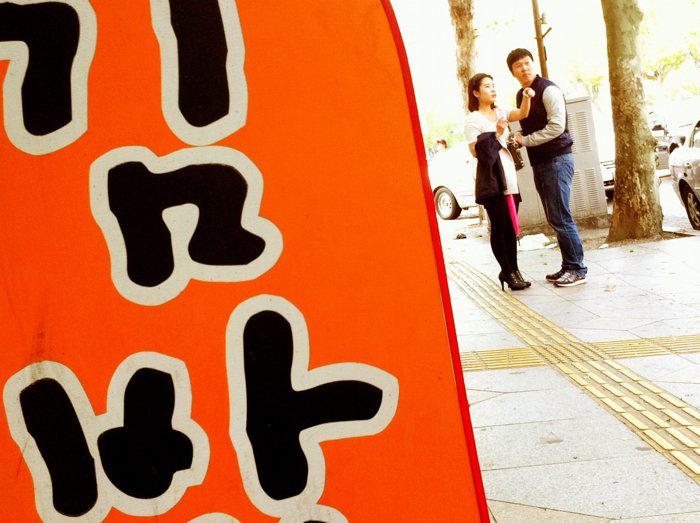 Una foto callejera en Corea del Sur con un letrero y una pareja.