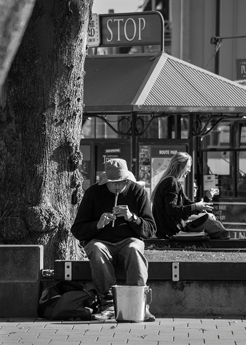 Retrato callejero en blanco y negro de un hombre tocando una flauta al aire libre en un día soleado - iluminación de fotografía callejera