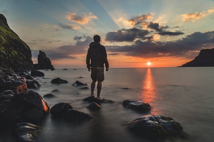 hombre parado en la orilla del mar con una puesta de sol en el fondo
