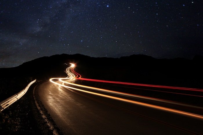 usando una calculadora de lapso de tiempo para fotos de lapso de tiempo: los rayos de luz de los autos en movimiento iluminan un camino oscuro durante la noche