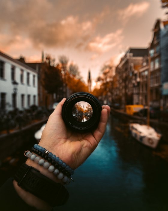 Fotografía creativa de una persona que sostiene una lente de cámara frente a la cámara en Groenburgwal, Amsterdam