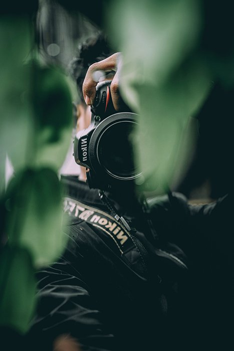 Un fotógrafo disparando a través de hojas verdes con una Nikon DSLR