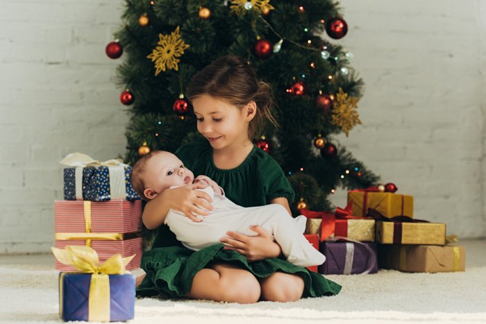 Una niña sosteniendo a un bebé recién nacido para su primera sesión de fotos navideña