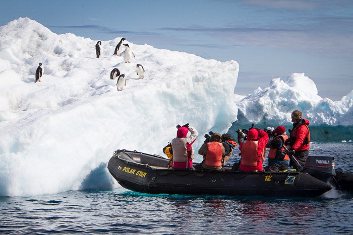 Un grupo de personas en una balsa fotografiando pingüinos en un iceberg
