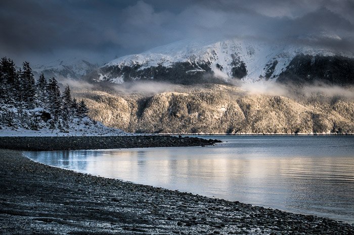 Fotografía costera: costa rocosa con una montaña cubierta de nieve al fondo