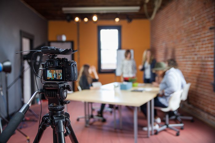 Una sesión de fotografía comercial configurada con una cámara dslr en un trípode en primer plano, fondo borroso de personas alrededor de una mesa