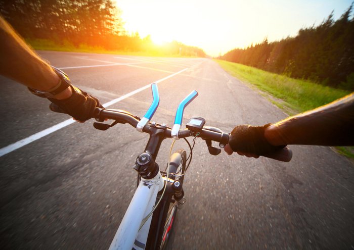 Las manos del ciclista con guantes en el manillar de una bicicleta montando en una carretera de asfalto borrosa en movimiento