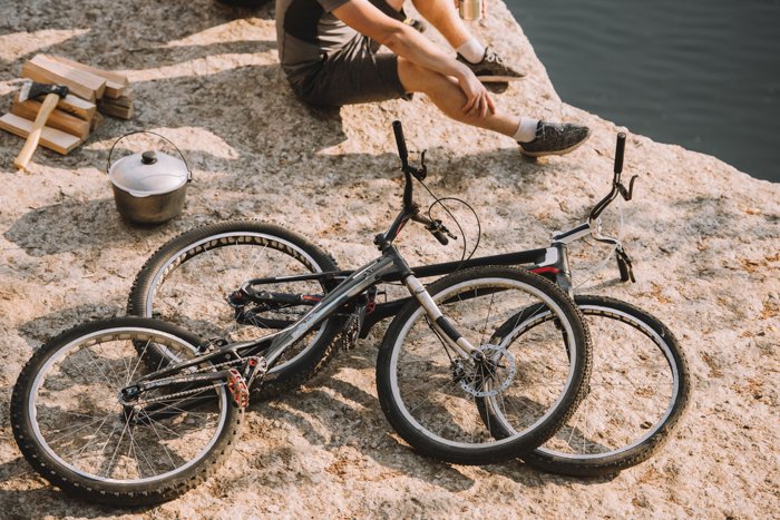 Composición fotográfica recortada de un hombre sentado sobre rocas junto a dos bicicletas