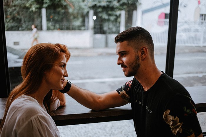 un hombre sosteniendo suavemente la cara de su novia junto a una ventana
