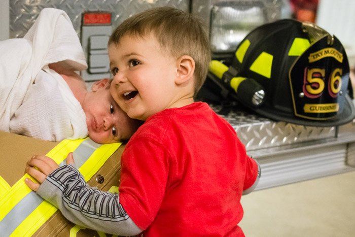 Un retrato familiar de un niño pequeño y un bebé recién nacido posaron con parafernalia de bombero