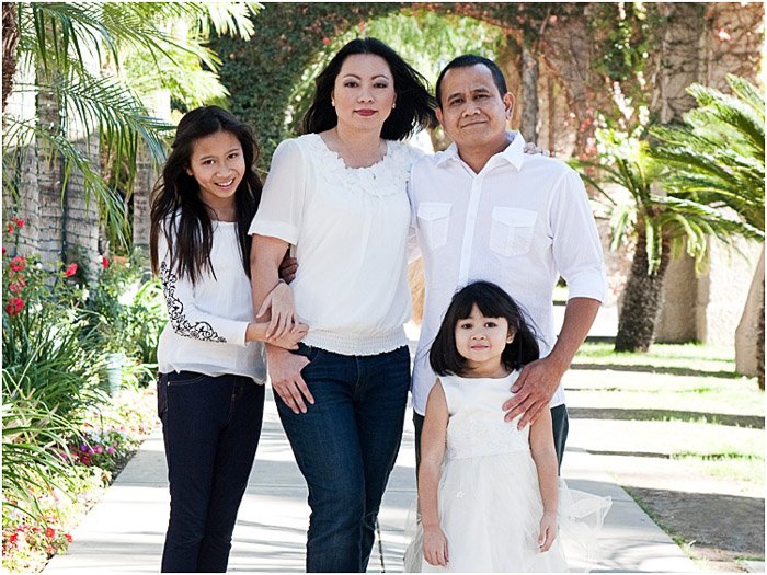Una familia de cuatro personas posando al aire libre con luz moteada