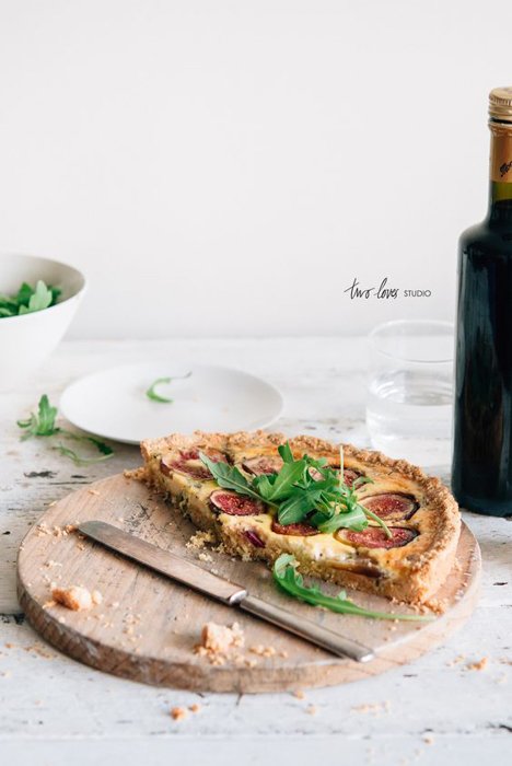 media pizza en una bandeja de madera sobre una mesa blanca con hierbas encima junto a un cuchillo, una botella de vino sobre la mesa