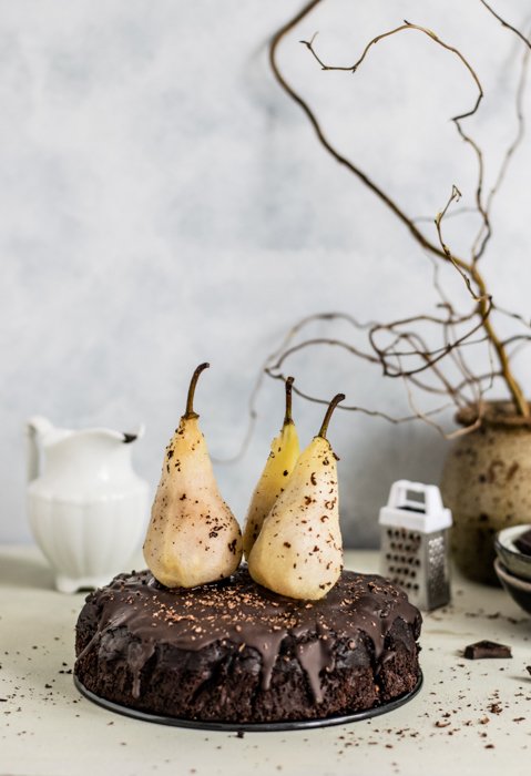 tres peras encima de un pastel de chocolate, una planta seca al fondo