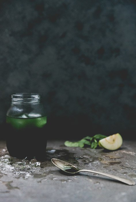 Consejos de diseño de alimentos: una naturaleza muerta con una bebida verde en un frasco junto a una cucharilla e ingredientes sobre un fondo oscuro