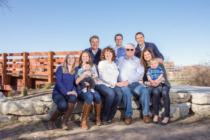 Una foto de grupo familiar al aire libre en un día brillante, familia con jeans y botas, un puente de madera y un cielo azul detrás de ellos