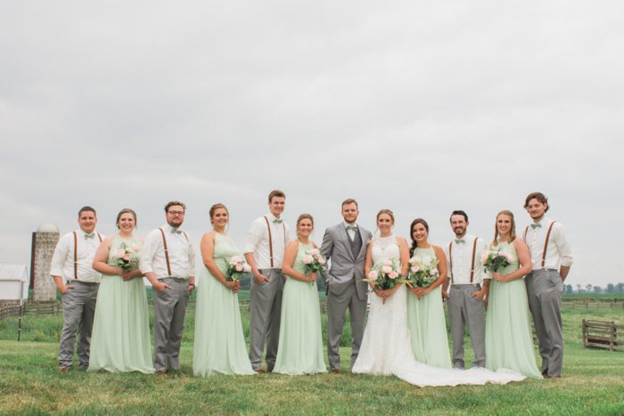 Un séquito de bodas posando en un campo de hierba, damas de honor con vestidos de color menta, padrinos de boda con tirantes