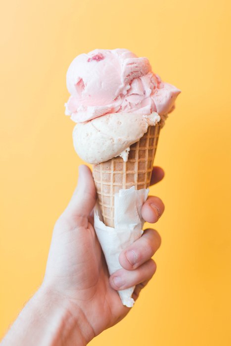 Mano sosteniendo un helado de fresa frente a un fondo amarillo