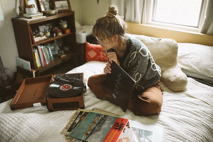 Un retrato de fotografía analógica de una niña sentada en su cama eligiendo discos de vinilo para jugar en una habitación acogedora - retratos de estilo de vida