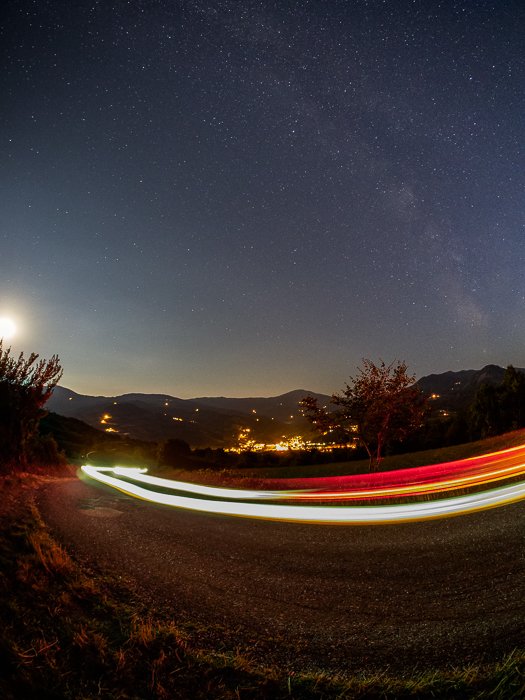 Un paisaje nocturno que incluye estelas de luz de mi automóvil que circula por la carretera frente a mí.