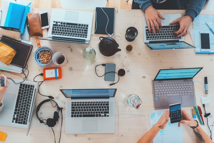 Fotografía cenital de 5 computadoras portátiles en un escritorio de oficina desordenado
