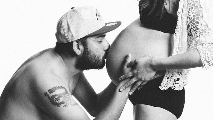 Foto de boudoir de maternidad en blanco y negro de un hombre besando el vientre de su esposa embarazada