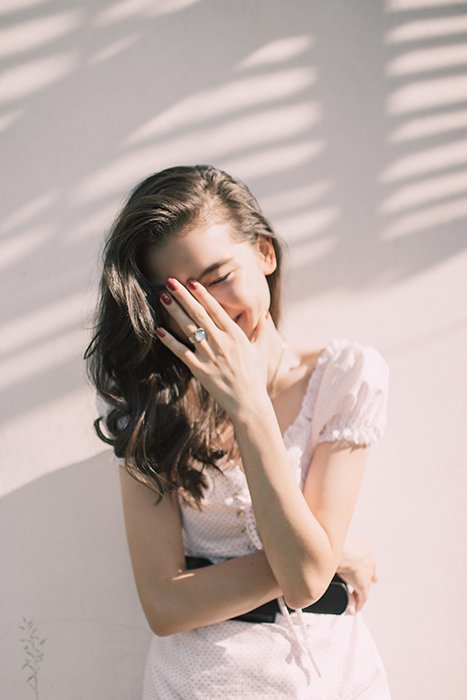 un retrato minimalista de una modelo femenina que cubre su rostro sonriente con la mano