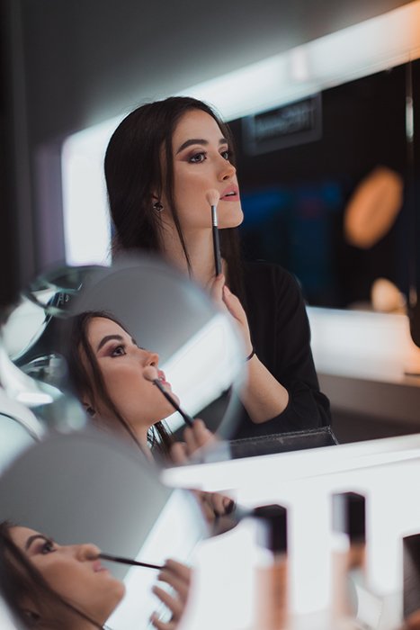 Un retrato díptico de una modelo morena reflejada en varios espejos mientras se maquilla