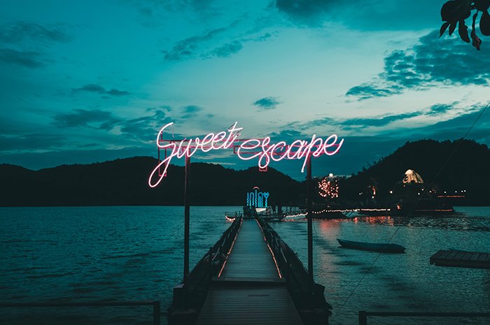 Luces de neón que dicen "dulce escape" en un puerto tranquilo