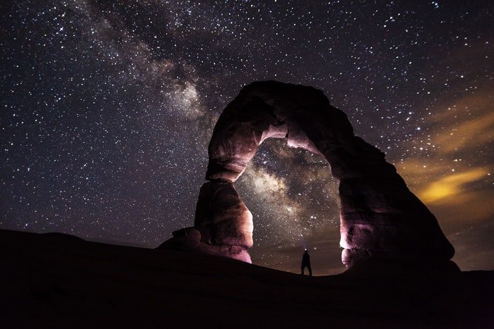 Una impresionante fotografía nocturna con un hombre bajo un arco de piedra y un cielo estrellado