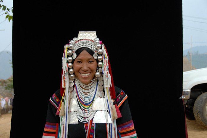 Una mujer con traje tradicional posa contra un fondo negro de tela colgada de un árbol en Ma Salong en un estudio de fotografía de retratos al aire libre.