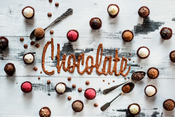 Chocolate de palabra hecho de glaseado con chocolates, dulces y cucharas de té sobre un fondo de madera blanca.  Concepto de tipografía de alimentos.  Dulce flatlay.