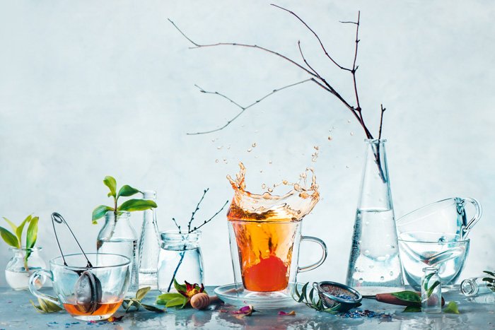 Taza de té con un toque dinámico y botellas de vidrio con plantas verdes y ramas de árboles en un bodegón de primavera de alta clave.  Concepto de limpieza y frescura.