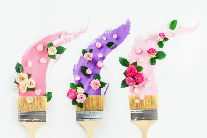 Pinceles con pinturas en tonos rosas y violetas, rosas y pétalos, sobre un fondo blanco.  Pintura primavera creativa puesta plana.  Concepto de decoración del hogar.