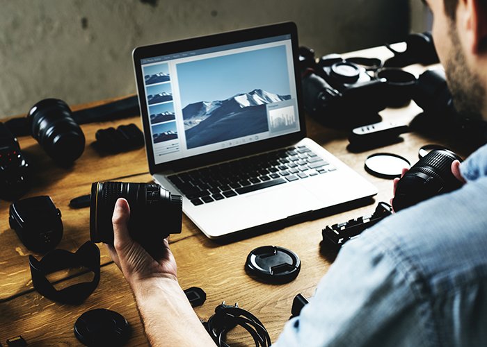 Fotógrafo editando en su escritorio lleno de cámaras.