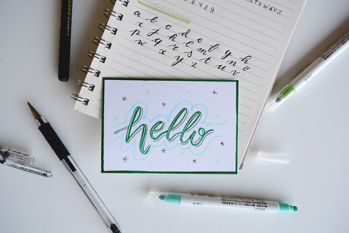 Un plano de papelería que incluye un cuaderno con la palabra 'hola' escrita en él