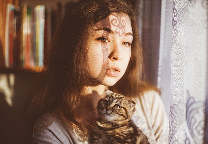 Un retrato de una modelo femenina sosteniendo un gato junto a una ventana - proyectos de fotografía