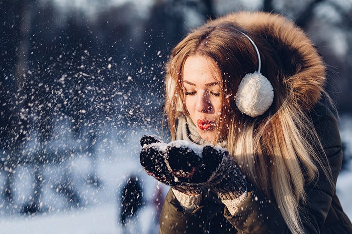 Cerrar la fotografía de retrato de invierno de una modelo femenina posando juguetonamente en la nieve que cae