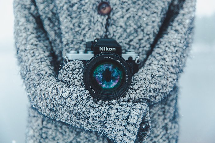Un primer plano de una cámara Nikon alrededor del cuello de un fotógrafo, fotografiando retratos en la nieve