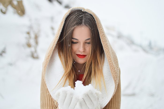 Cerrar la fotografía de retrato de invierno de una modelo femenina posando en la nieve que cae